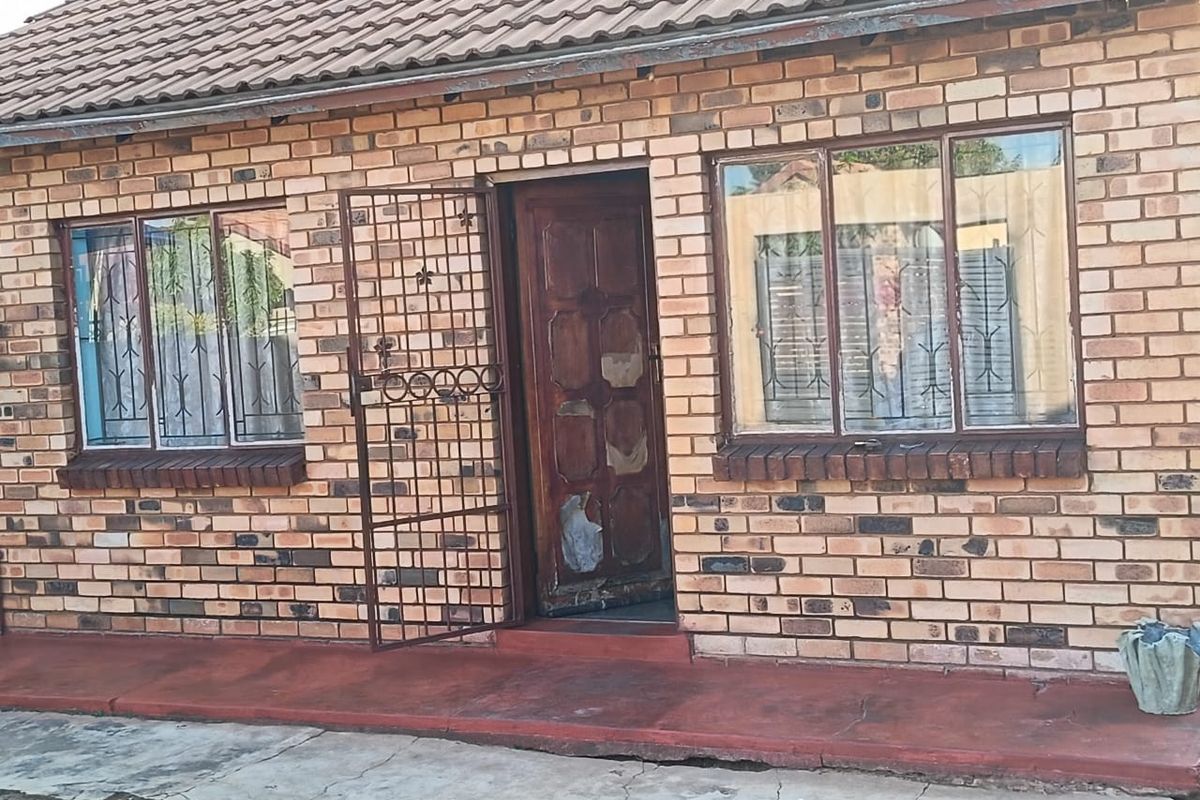 Front elevation of a face brick house featuring a tiled roof, security gate, and timber entrance door with visible wear.