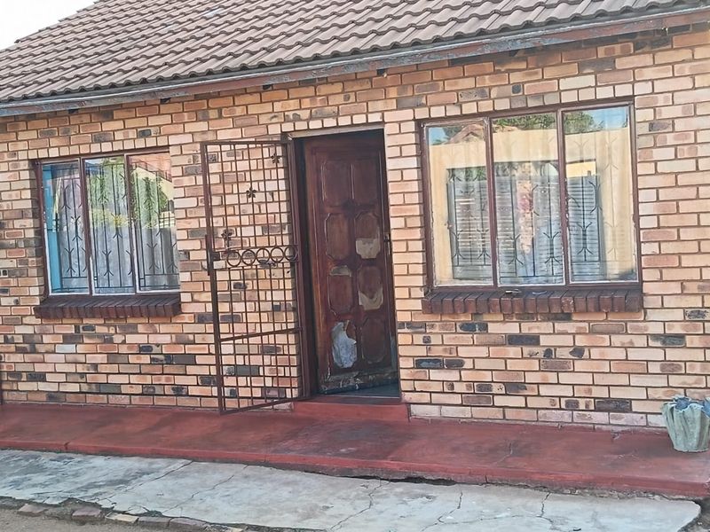 Front elevation of a face brick house featuring a tiled roof, security gate, and timber entrance door with visible wear.