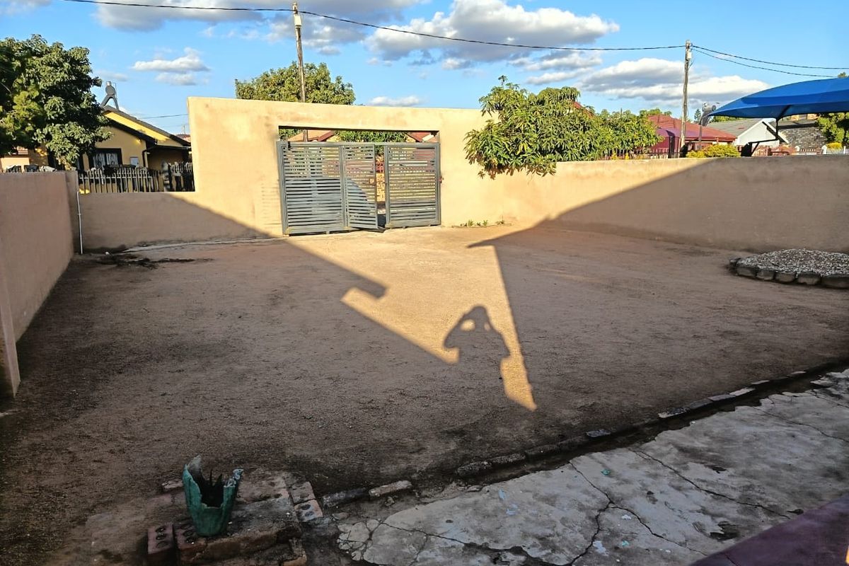 A spacious rear yard featuring a perimeter wall, metal gate, and a combination of concrete paving and unlandscaped ground.