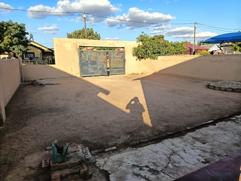 A spacious rear yard featuring a perimeter wall, metal gate, and a combination of concrete paving and unlandscaped ground.