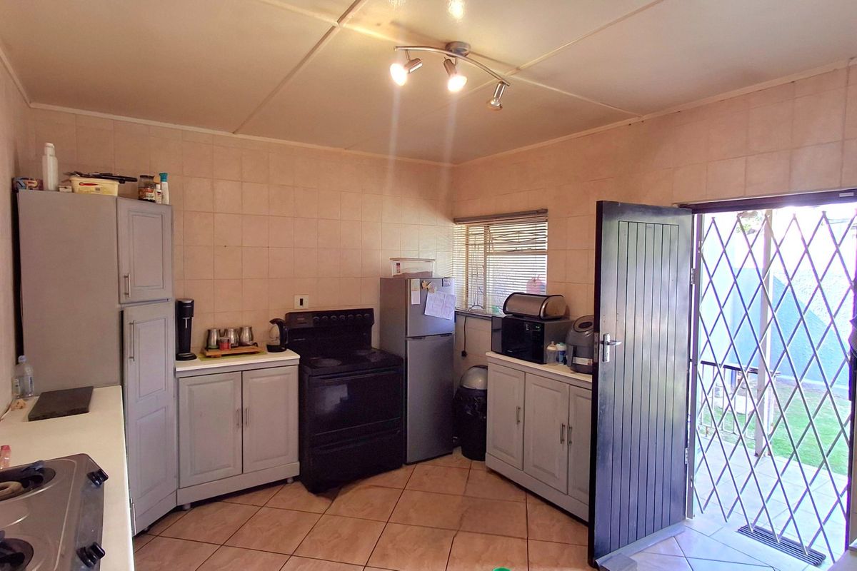A functional kitchen featuring tiled walls and flooring, built-in cabinetry, and direct access to the exterior through a security gate.