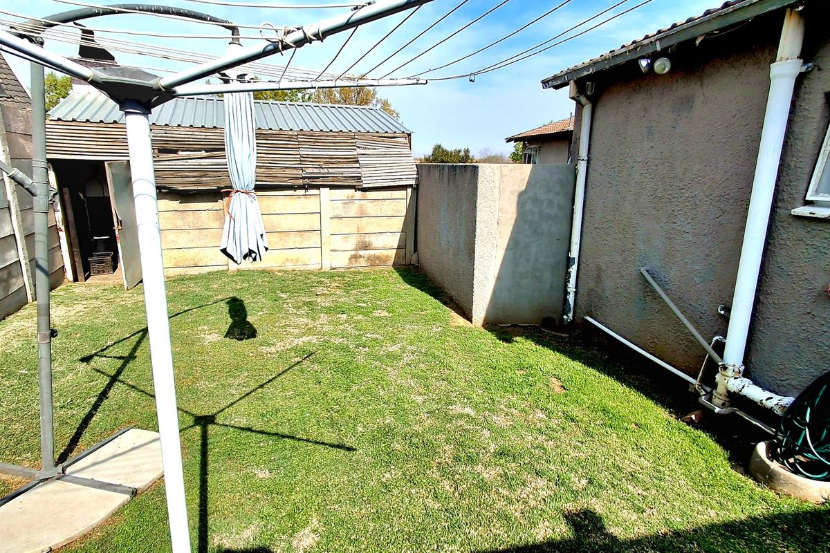A rear garden area featuring a lawn, precast concrete boundary walls, and a small corrugated metal storage shed.
