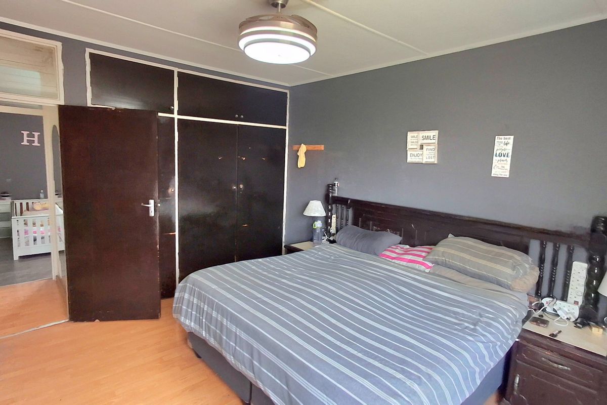 A bedroom featuring dark built-in cupboards, laminate flooring, and a central ceiling light fixture, with an adjoining room visible through the doorway.