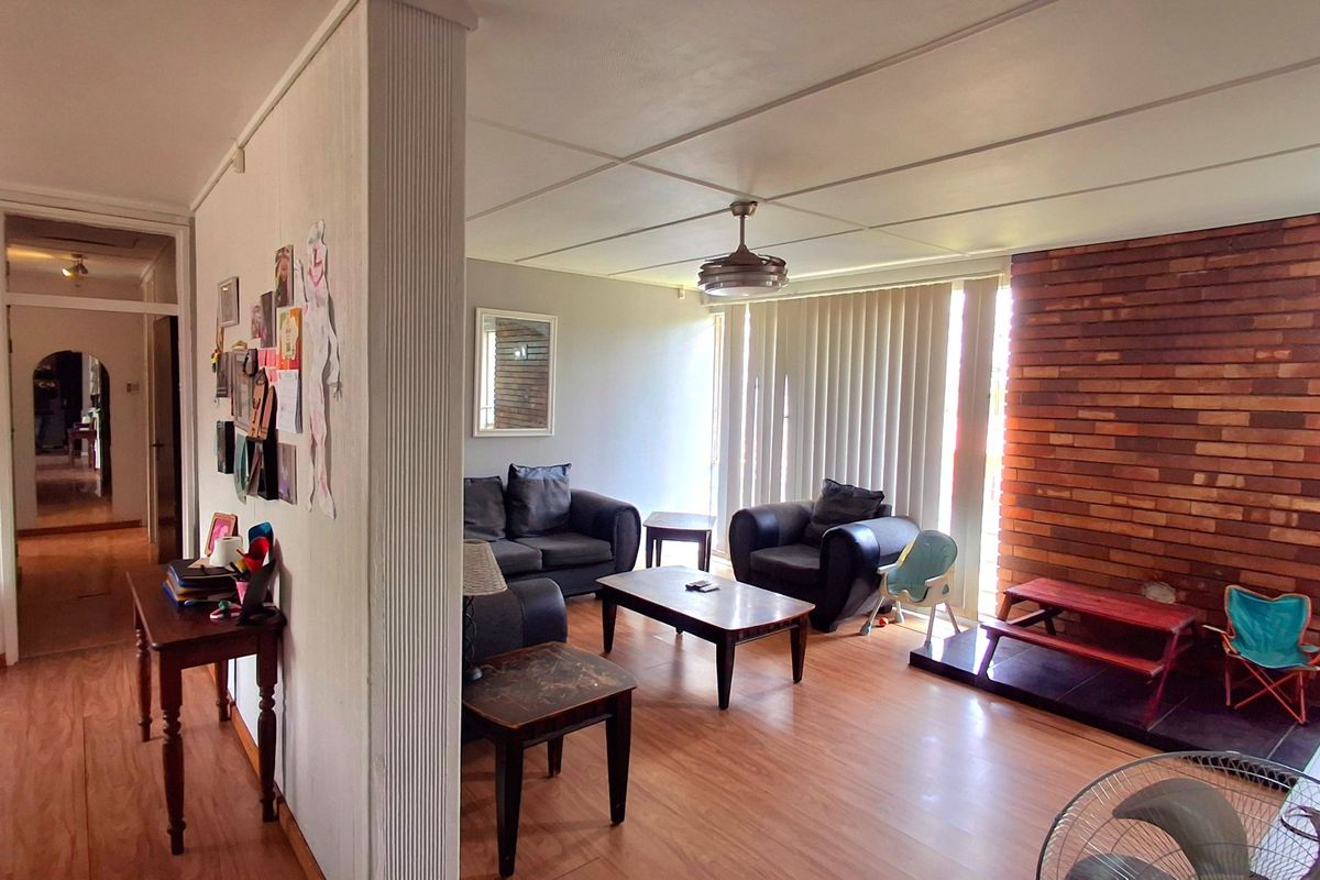 Spacious living room featuring an exposed brick feature wall, laminate flooring, and a ceiling fan, offering a comfortable and functional living space.