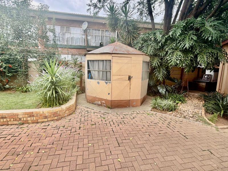 Rear garden area featuring brick paving, a landscaped retaining wall, and a detached storage shed in need of maintenance.