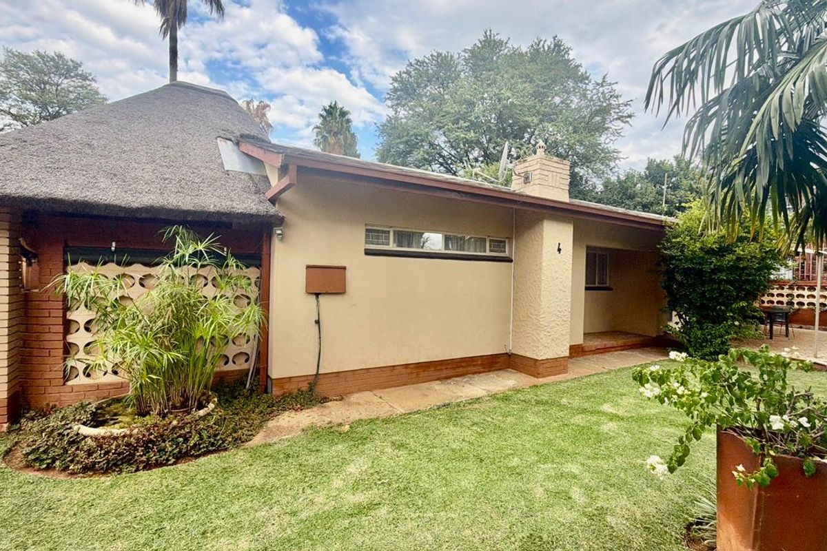Rear view of a house featuring a traditional thatched roof, brick chimney, and a private garden area with a concrete walkway.