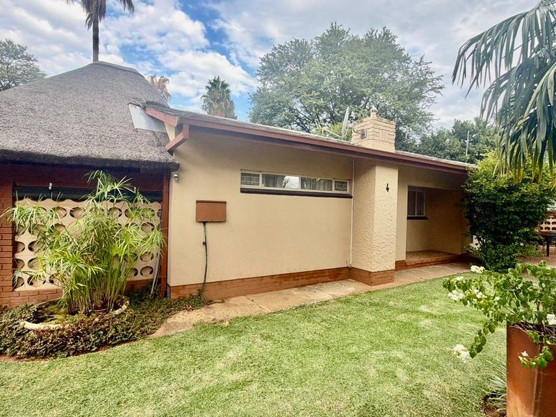 Rear view of a house featuring a traditional thatched roof, brick chimney, and a private garden area with a concrete walkway.