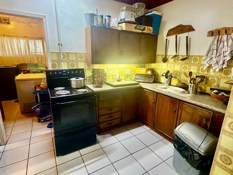 A functional kitchen featuring dated cabinetry, a tiled backsplash, and ceramic flooring, offering potential for a modern renovation to enhance the space.