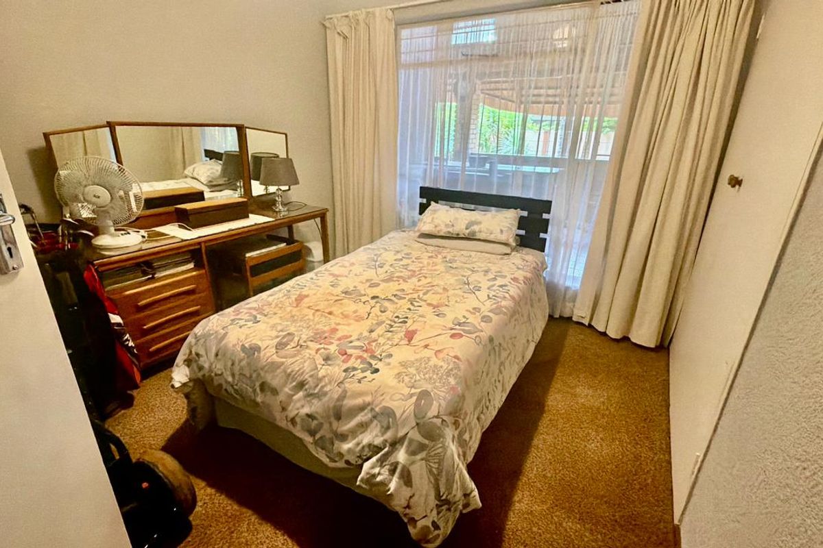 A functional bedroom featuring carpeted flooring, a built-in cupboard, and a large window providing natural light.