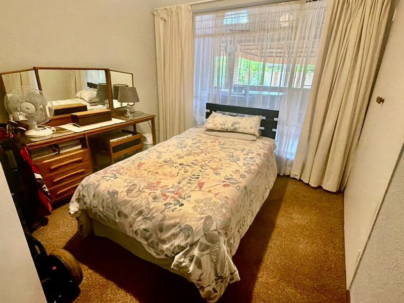 A functional bedroom featuring carpeted flooring, a built-in cupboard, and a large window providing natural light.