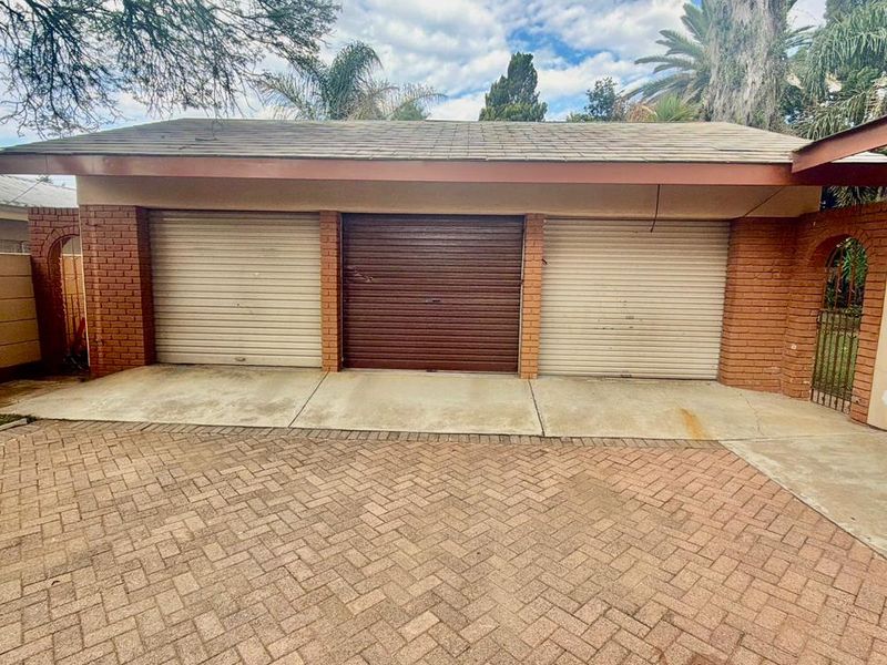 A triple garage featuring roller shutter doors and a paved driveway, set against a brick and plaster exterior facade.