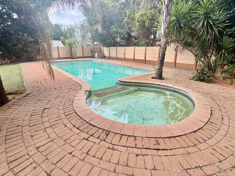 Outdoor pool area featuring a swimming pool with integrated steps, surrounded by brick paving and enclosed by a precast concrete boundary wall.