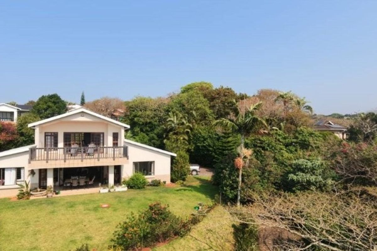 Aerial view of the rear elevation featuring a spacious lawn, a covered ground-floor patio, and an upper-level balcony overlooking the garden.