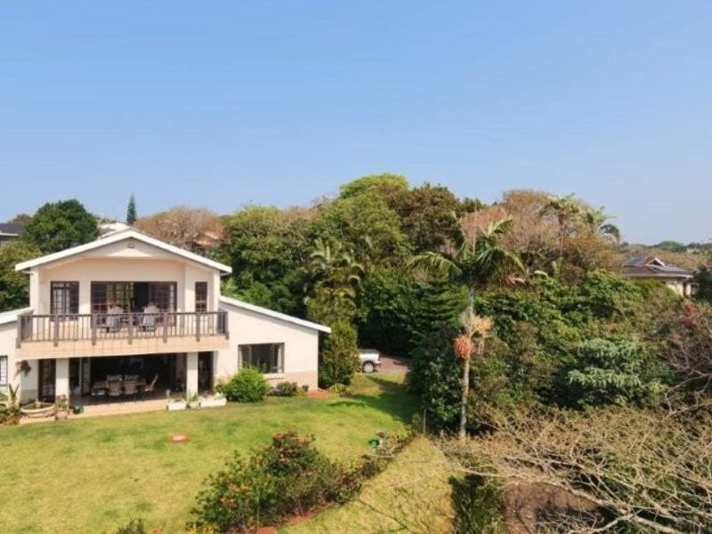 Aerial view of the rear elevation featuring a spacious lawn, a covered ground-floor patio, and an upper-level balcony overlooking the garden.