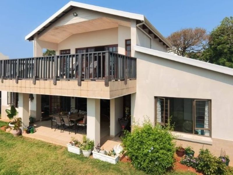 Rear view of the house featuring a spacious upper-level balcony with timber railings and a covered ground-floor patio overlooking the garden.