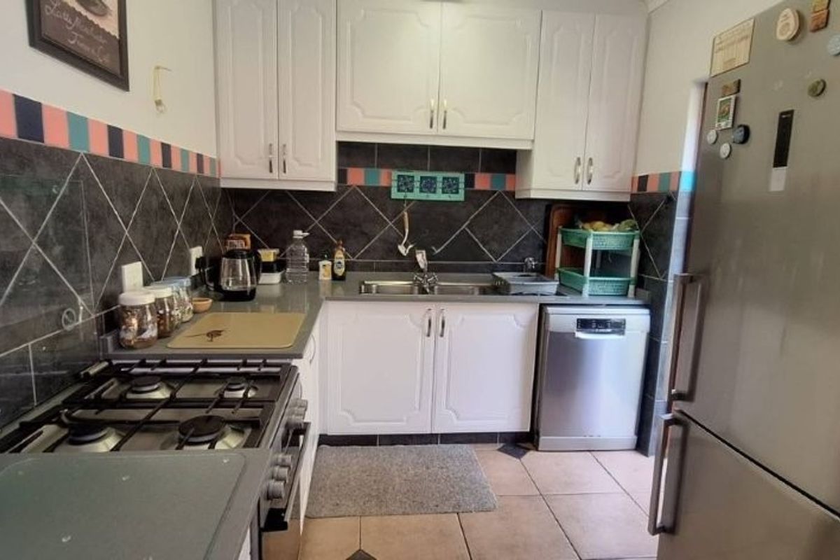 A functional kitchen featuring white cabinetry, a gas hob, oven, double sink, and dark tiled backsplash with neutral floor tiles.