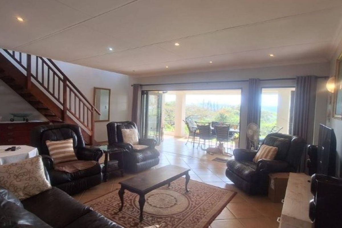 Spacious living room featuring tiled flooring, recessed lighting, and a staircase, with large sliding glass doors opening to an outdoor patio area.