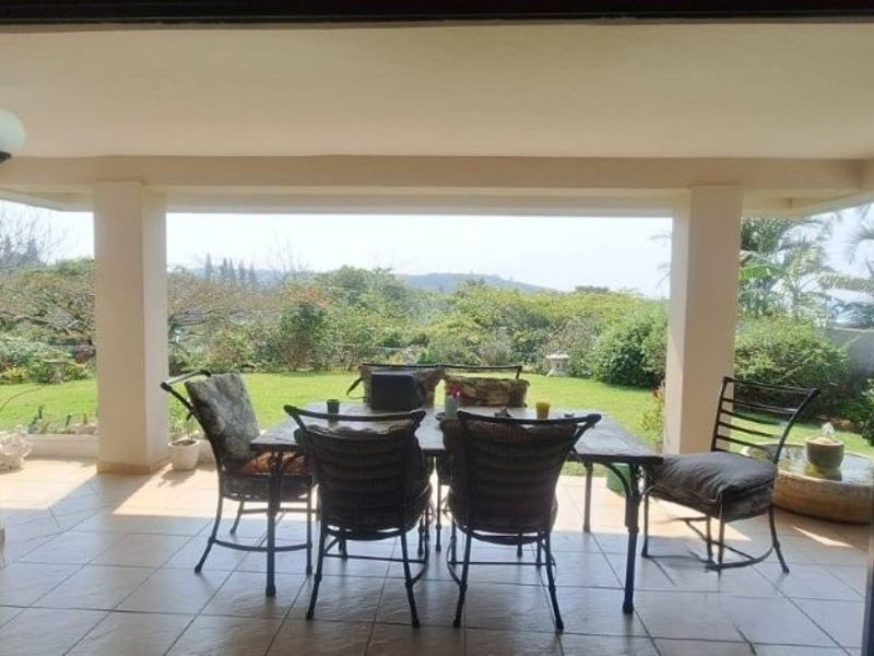 A covered patio area featuring tiled flooring and structural columns, offering a seamless transition to the garden and scenic outdoor views.