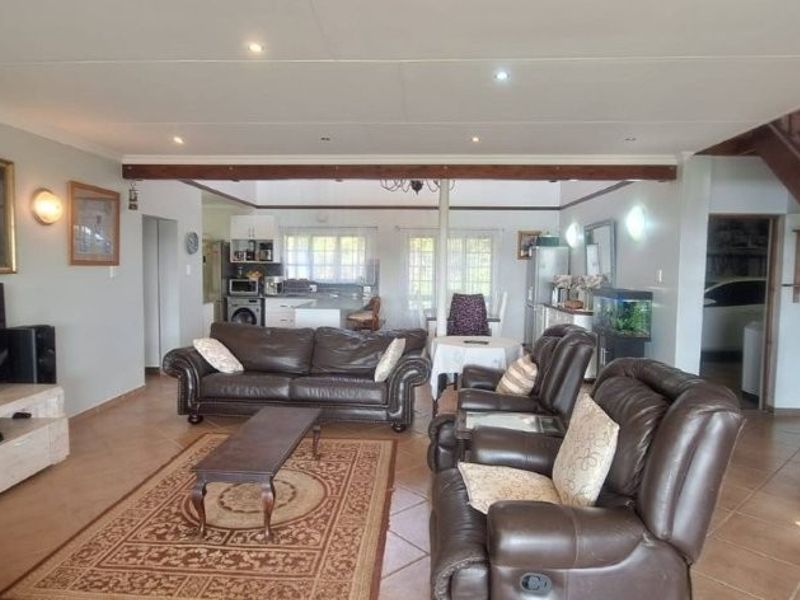 Spacious open-plan living area featuring tiled floors, recessed lighting, and a wooden staircase, seamlessly connecting to the kitchen space.