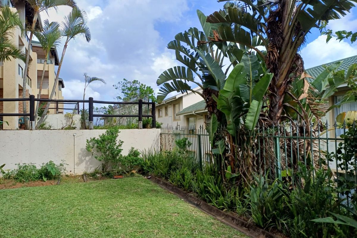 A private rear garden area featuring a well-maintained lawn, established landscaping, and secure metal perimeter fencing within an apartment complex setting.