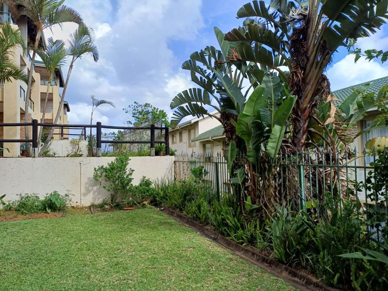 A private rear garden area featuring a well-maintained lawn, established landscaping, and secure metal perimeter fencing within an apartment complex setting.
