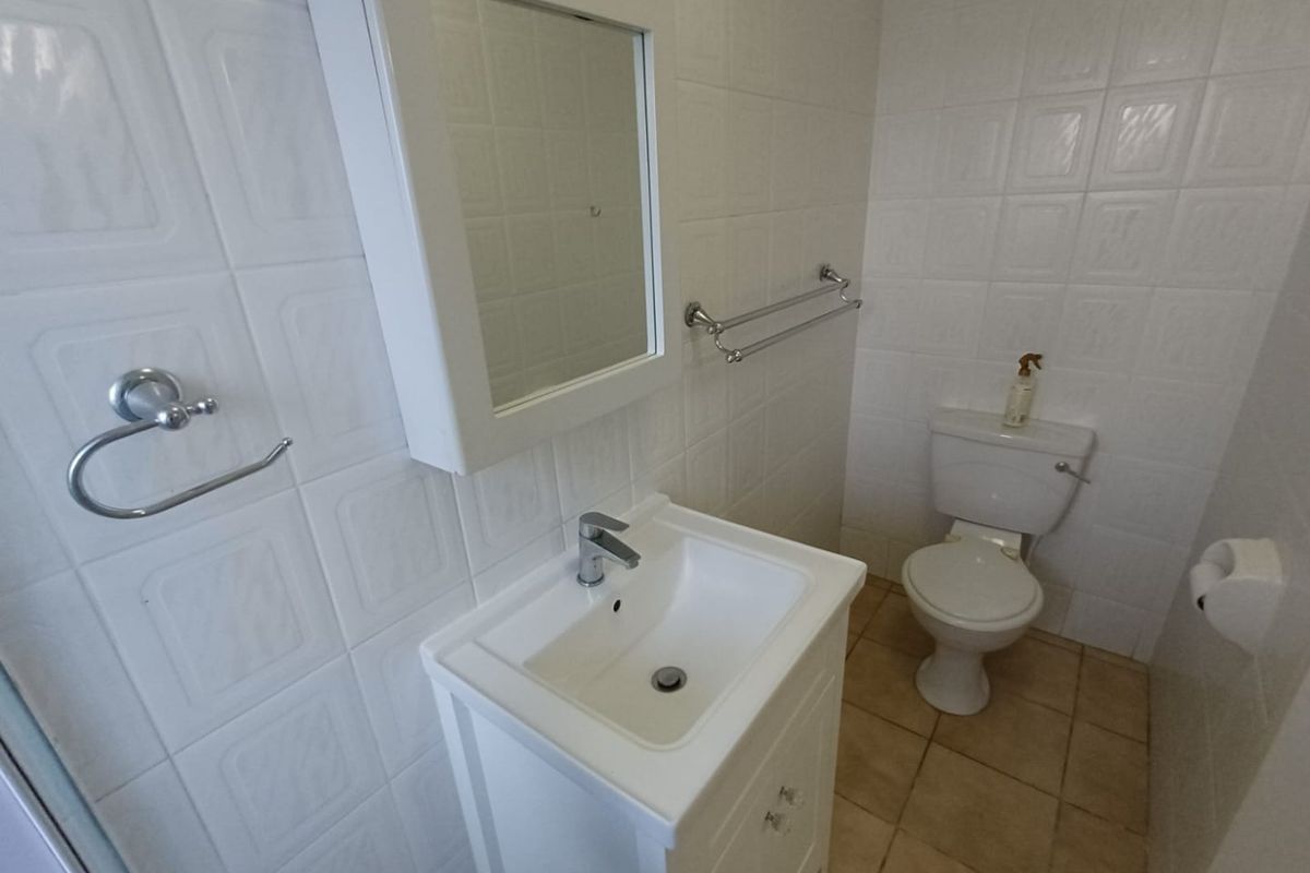 A functional bathroom featuring a vanity cabinet with basin, wall-mounted mirror cabinet, toilet, and tiled finishes throughout.