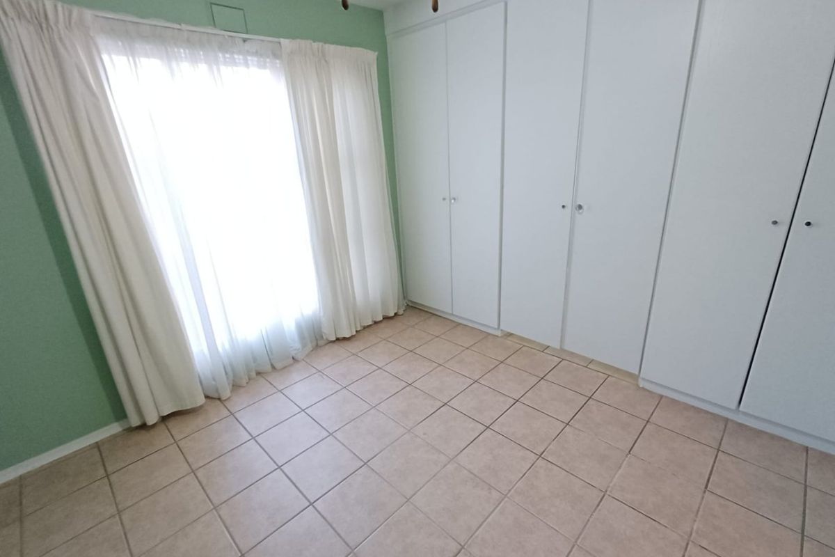 A bright, empty bedroom featuring neutral tiled flooring and extensive built-in cupboard storage with access to a sliding door.