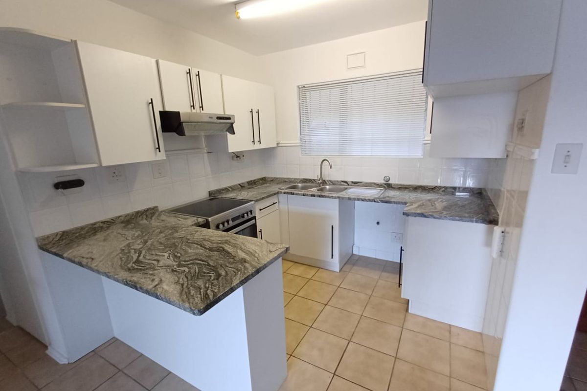 A functional kitchen featuring white cabinetry, stone-look countertops, a stainless steel sink, and an integrated electric stove with an extractor fan.
