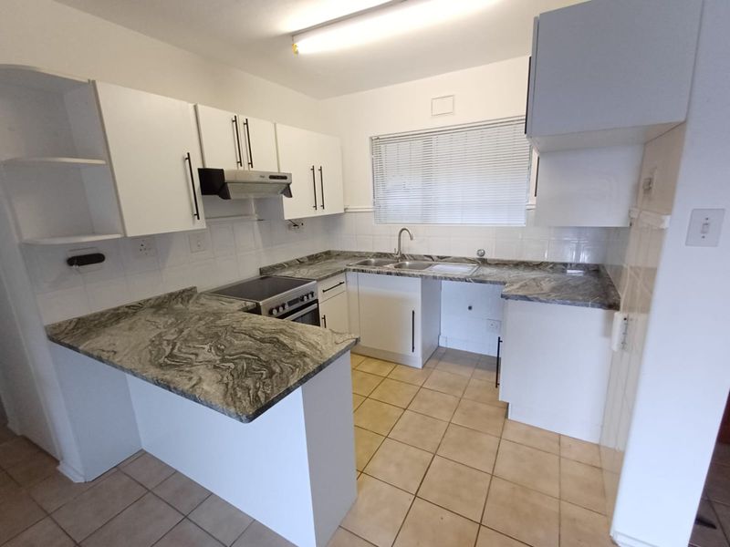 A functional kitchen featuring white cabinetry, stone-look countertops, a stainless steel sink, and an integrated electric stove with an extractor fan.