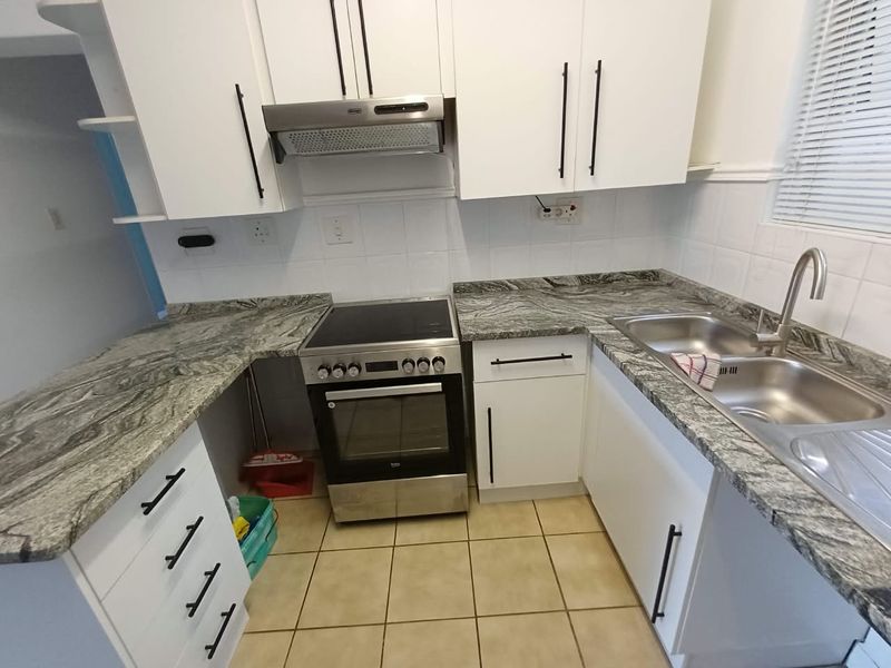 A functional kitchen featuring white cabinetry, granite countertops, a stainless steel double sink, and a built-in oven with an extractor fan.