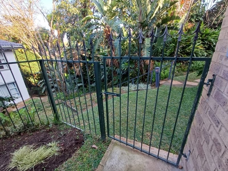 A secure wrought iron gate providing access to a well-maintained rear garden area with lush greenery and a paved pathway.