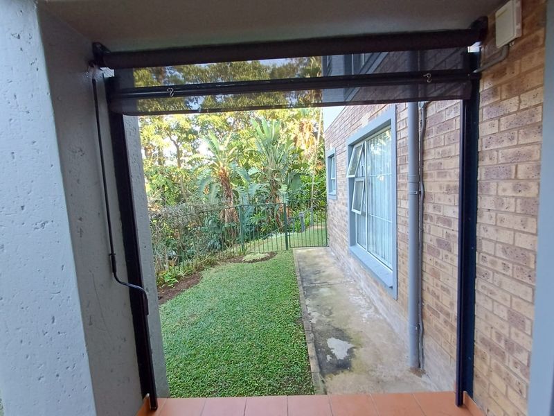 A covered patio area featuring tiled flooring and a retractable outdoor blind, overlooking a private garden space with a brick exterior wall.