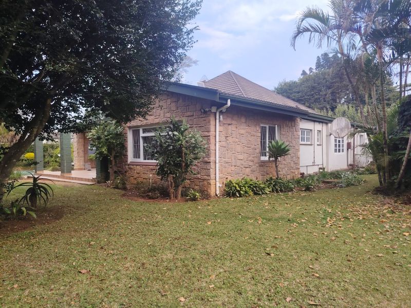 Rear view of a house featuring stone cladding, a tiled roof, and a covered patio area set within a landscaped garden.