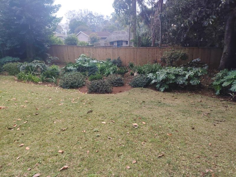 A private rear garden featuring a well-maintained lawn, established garden beds with mature shrubs, and a timber boundary fence.