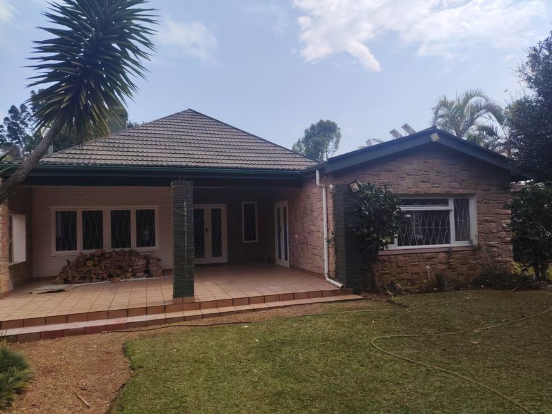 Rear view of the house featuring a covered tiled patio, stone cladding facade, and a well-maintained garden area.