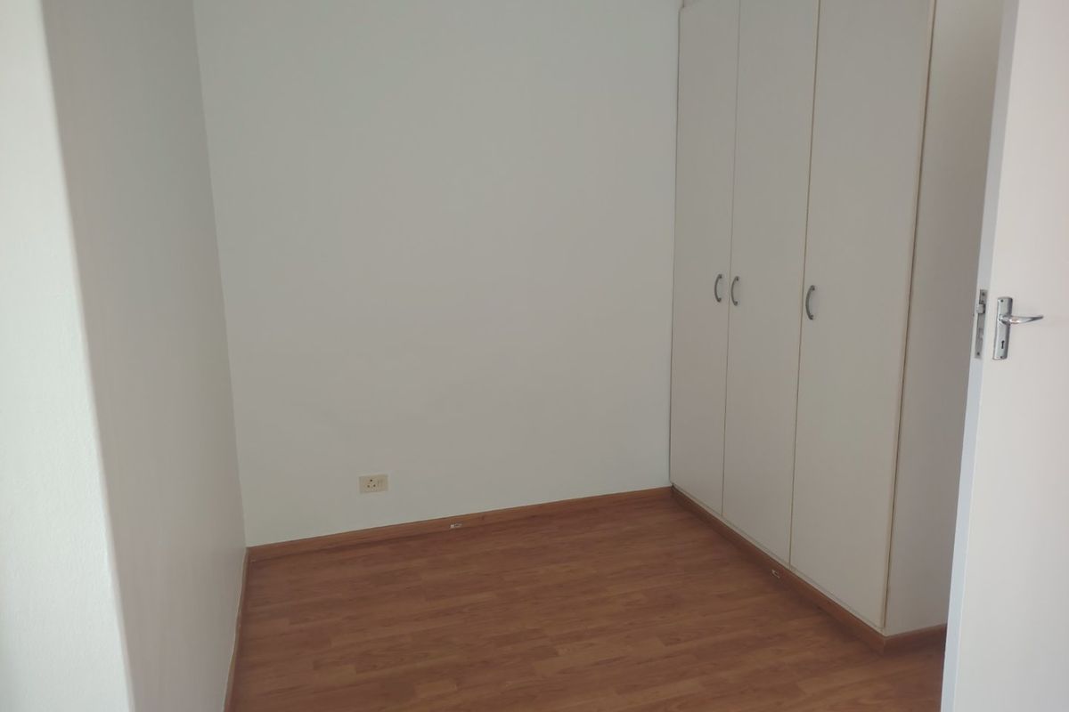 A clean, empty bedroom featuring light-toned laminate flooring and white built-in cupboards, offering a neutral space ready for personalization.