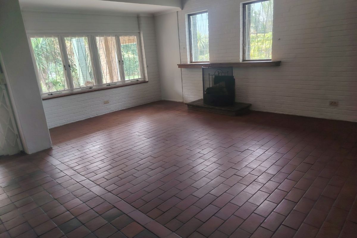 Spacious living room featuring traditional brick flooring, a built-in fireplace with a mantelpiece, and large windows with security bars.