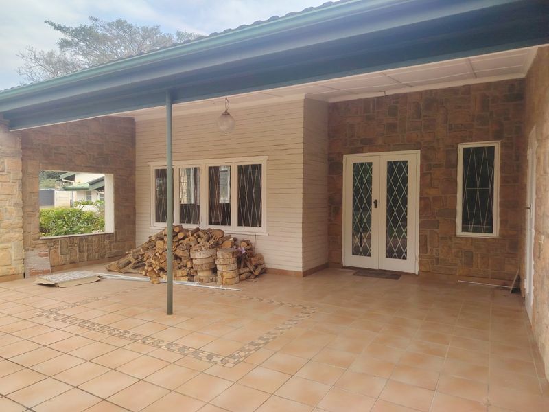 A spacious covered patio featuring stone cladding, tiled flooring, and double glass doors, providing a versatile outdoor entertainment area.