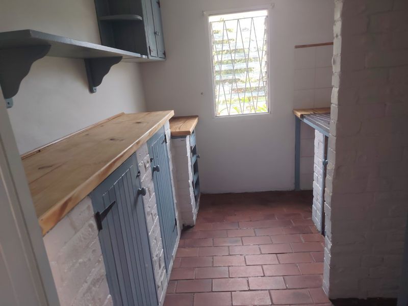 A functional scullery or utility area featuring brick-built cabinetry with wooden countertops, tiled flooring, and a secure louvre window.