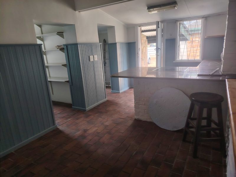 A functional kitchen area featuring brick flooring, beadboard wainscoting, built-in shelving, and a stone-topped breakfast bar with direct outdoor access.