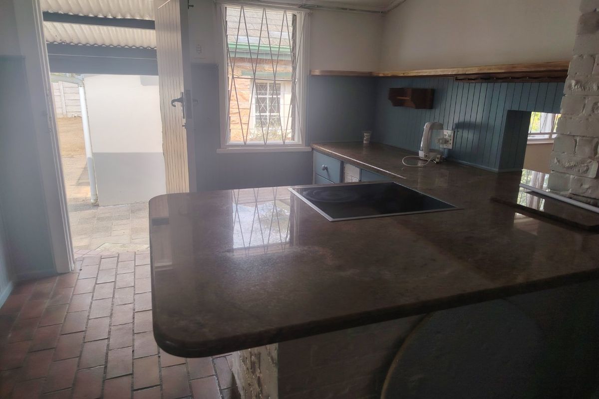 A functional kitchen area featuring a stone countertop with an integrated induction hob, brick flooring, and direct access to an outdoor patio area.