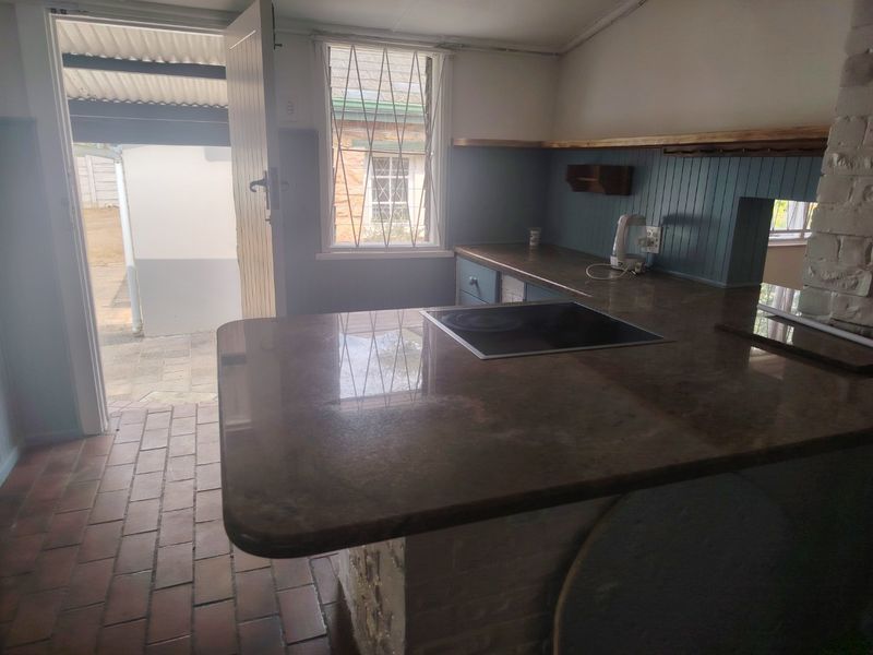 A functional kitchen area featuring a stone countertop with an integrated induction hob, brick flooring, and direct access to an outdoor patio area.