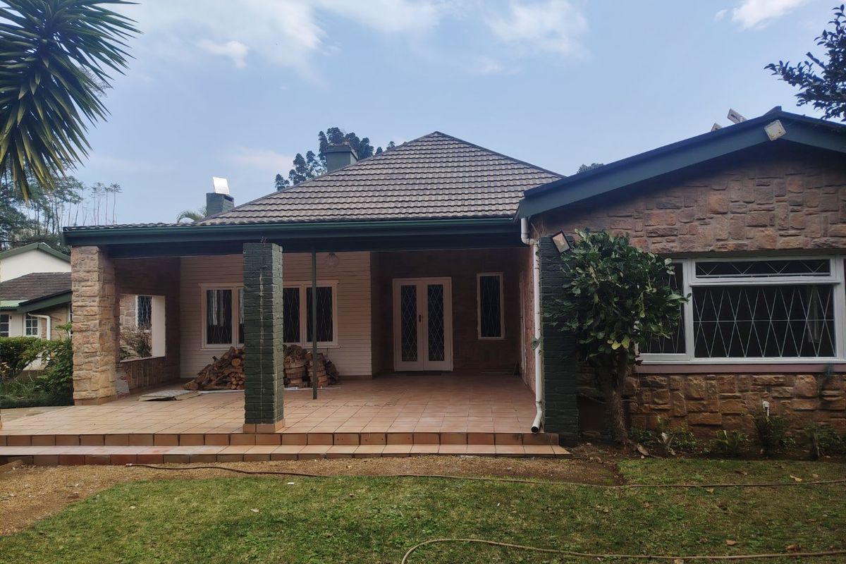 A rear view of the house featuring a covered tiled patio, stone facade, and a well-maintained garden area.