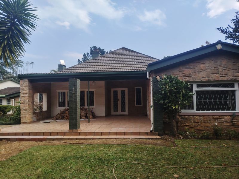 A rear view of the house featuring a covered tiled patio, stone facade, and a well-maintained garden area.