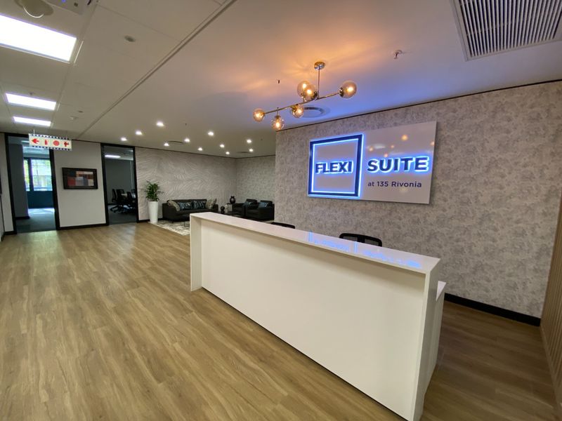 Modern commercial reception area featuring a sleek white desk, illuminated branding, wood-look vinyl flooring, and professional recessed and feature lighting.