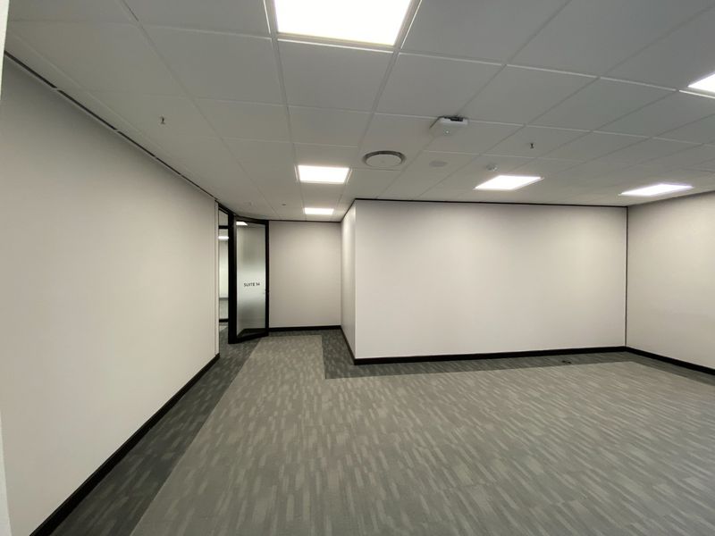 A clean, vacant commercial office suite featuring a suspended ceiling with recessed lighting, grey carpet tiles, and a modern glass entrance door.
