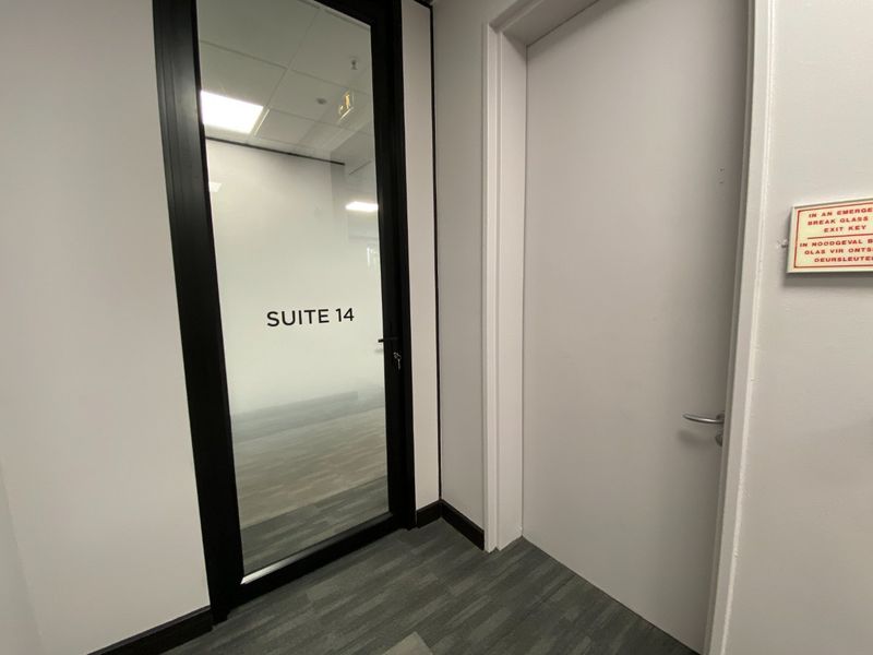 A clean commercial hallway featuring a glass-paneled door labeled Suite 14, adjacent to a standard door with an emergency exit key box.