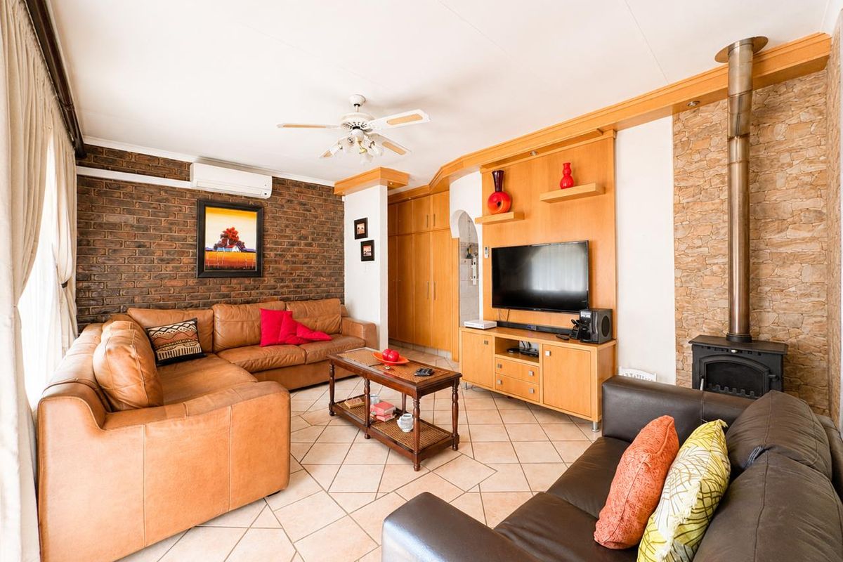 A cozy living room featuring an exposed brick wall, stone fireplace with a wood-burning stove, tiled flooring, and built-in cabinetry.