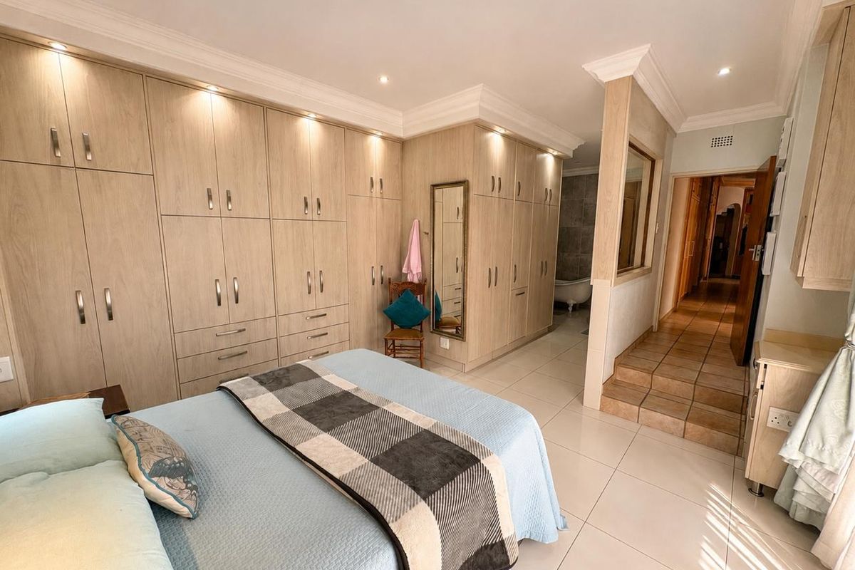 Spacious bedroom featuring extensive built-in cabinetry, tiled flooring, recessed lighting, and a raised transition area leading to an en-suite bathroom.