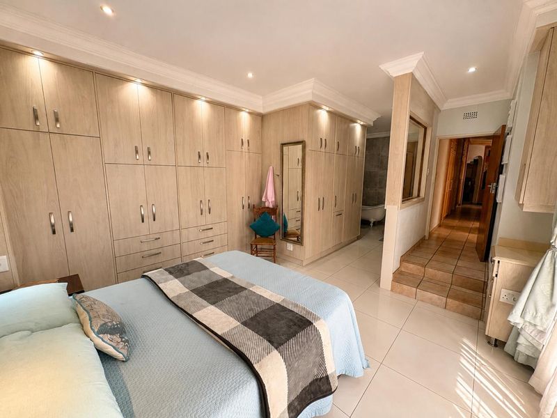 Spacious bedroom featuring extensive built-in cabinetry, tiled flooring, recessed lighting, and a raised transition area leading to an en-suite bathroom.